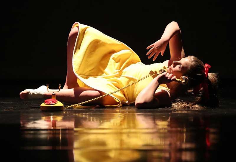 a performer in a yellow dress lies on the stage holding a phone during a dance concert